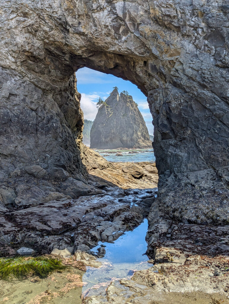 Natural rock arch frames sea stack at Rialto Beach, Olympic National Park, Washington during daylight hours with tide pools