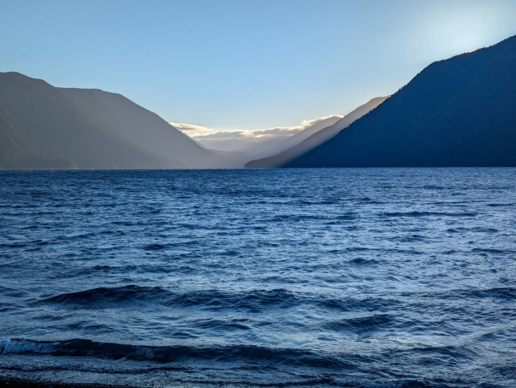Deep blue lake waters with mountain silhouettes creating dramatic shadows during golden hour light at Lake Crescent, Olympic National Park, Washington
