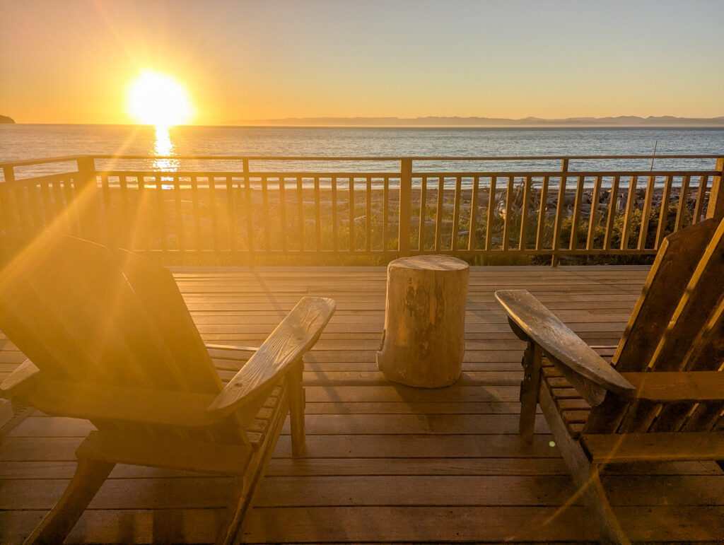 Wooden deck chairs and table on oceanfront balcony overlooking calm waters during golden hour sunset