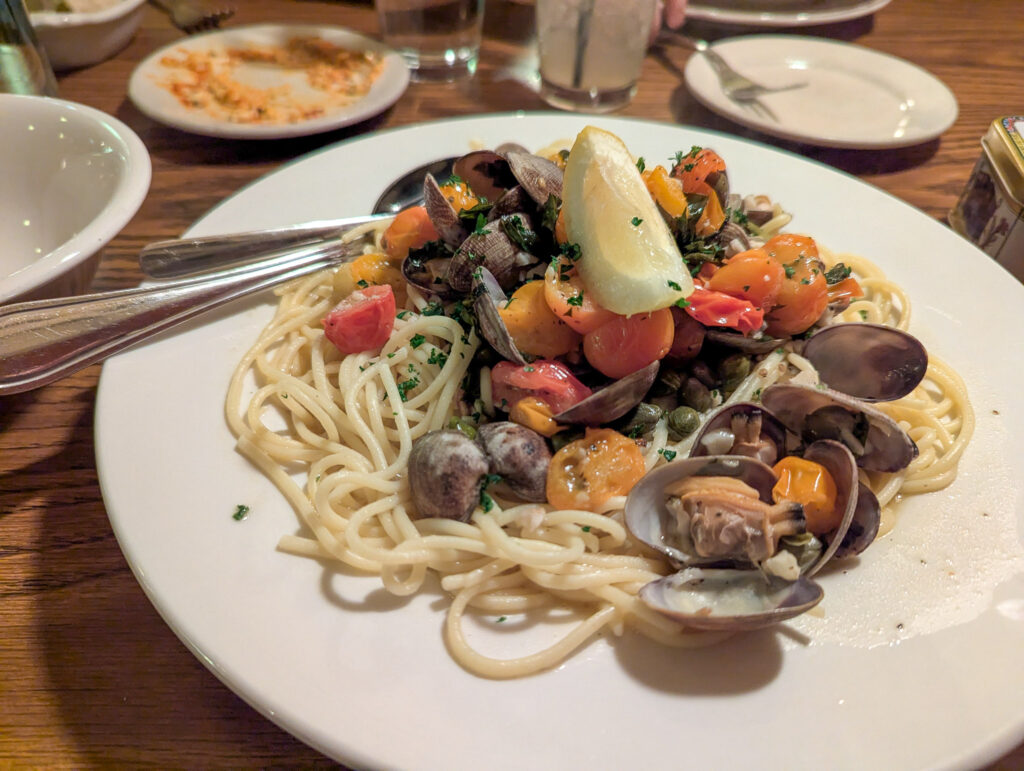 Seafood pasta dish with clams, mussels, tomatoes and linguine noodles served on white plate at restaurant table