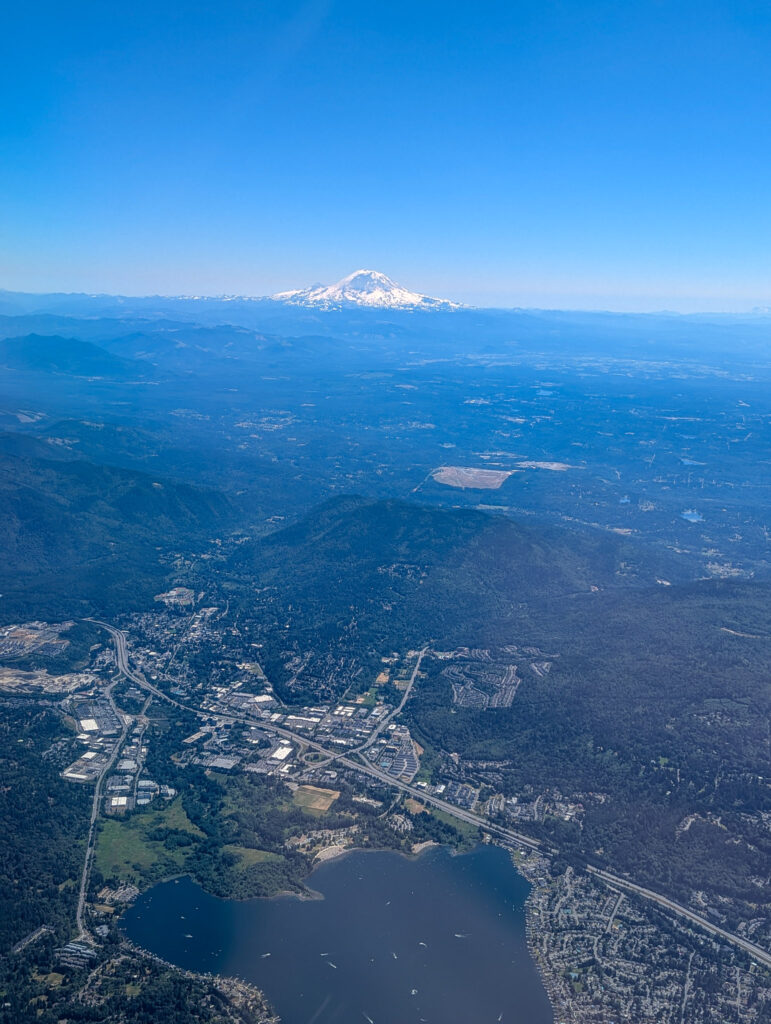 Aerial view of Mount Rainier rising above forested hills and a lake near Tacoma, Washington on a clear sunny day