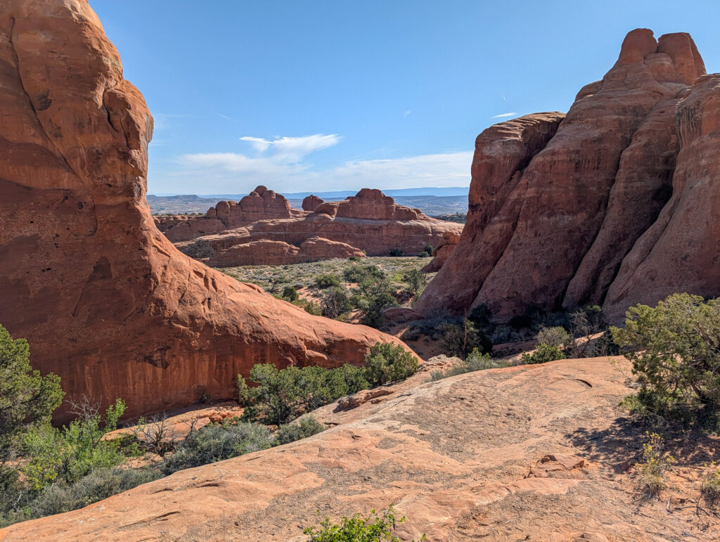 View through a gap between two towering red sandstone fins in Devil's Garden toward a juniper-dotted valley below.