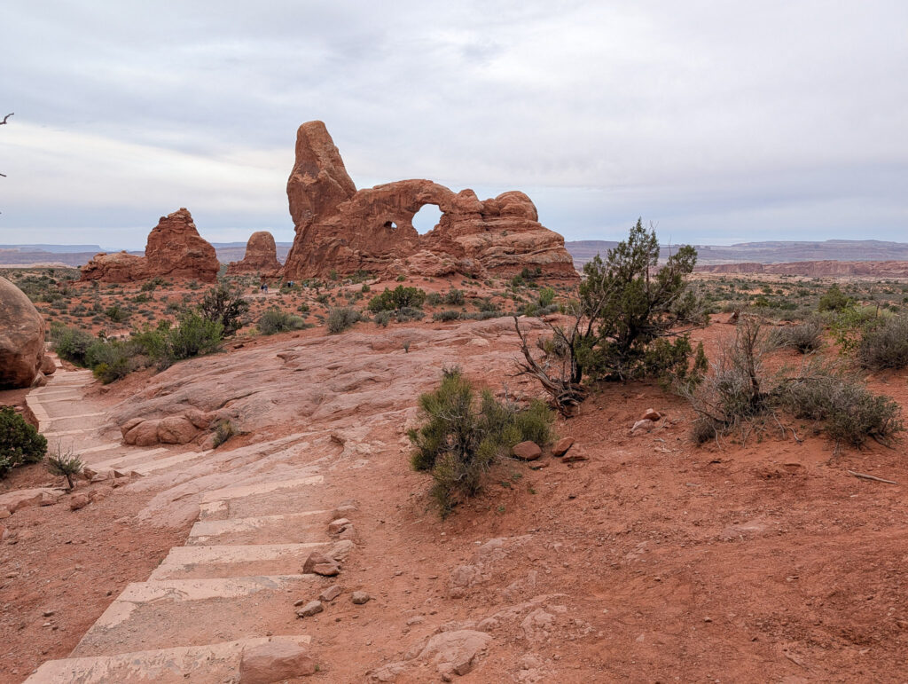 Stone slab steps on the Windows Loop Trail lead toward Turret Arch under a heavy overcast sky.