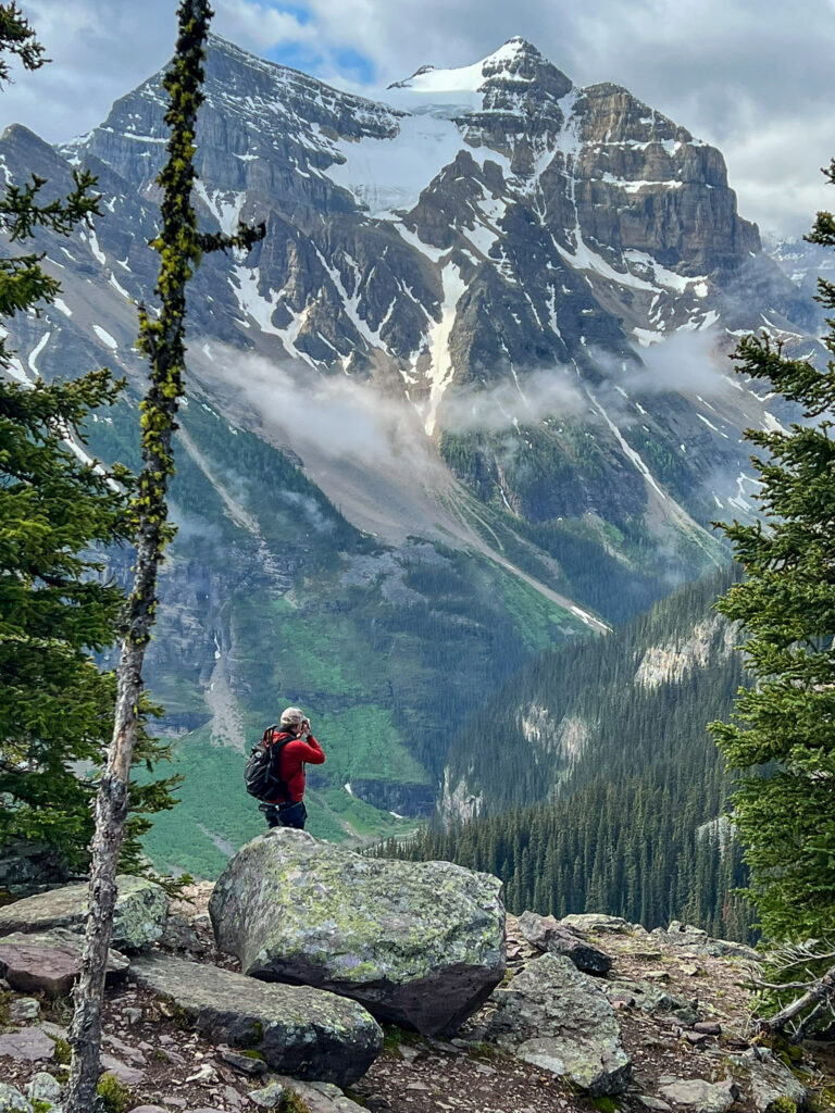 Hiker photographing Mount Robson from rocky outcrop in Mount Robson Provincial Park, British Columbia on cloudy day