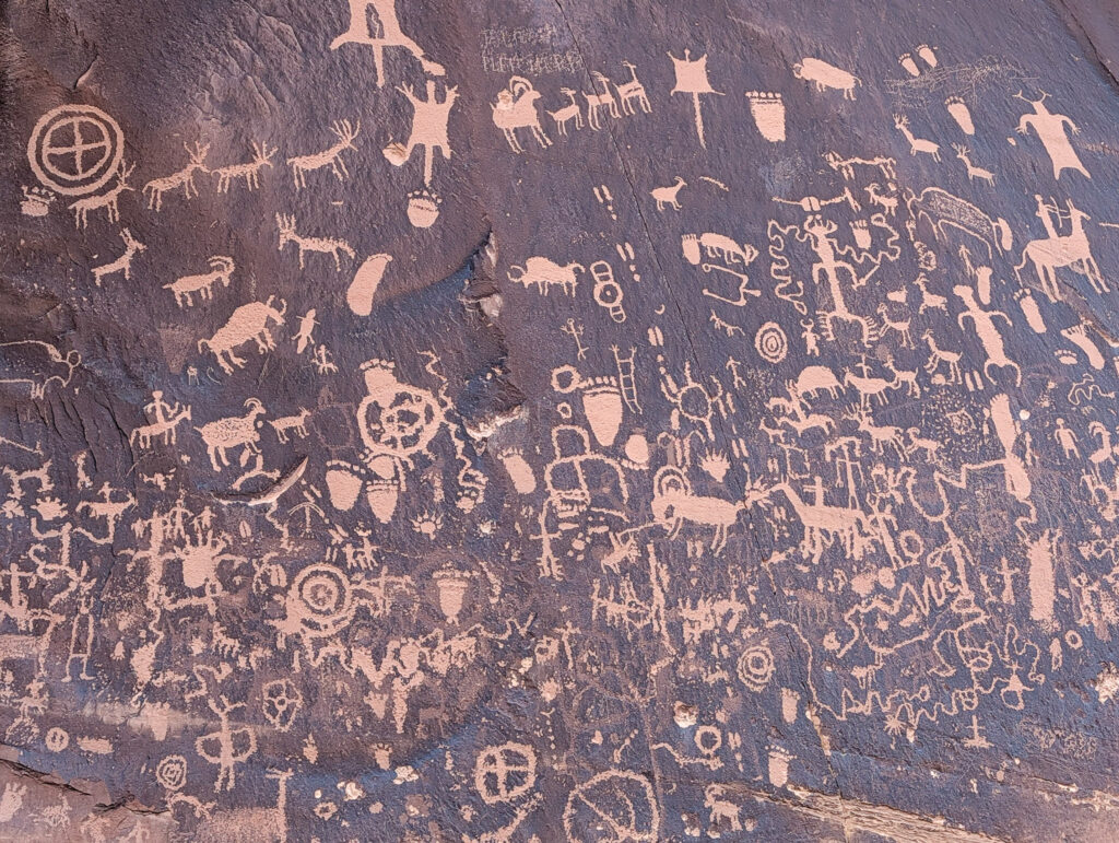 Newspaper Rock State Historic Monument displays a dense sandstone panel of Ancestral Puebloan and Navajo petroglyphs, including bighorn sheep, human figures, and spirals carved into dark desert varnish.