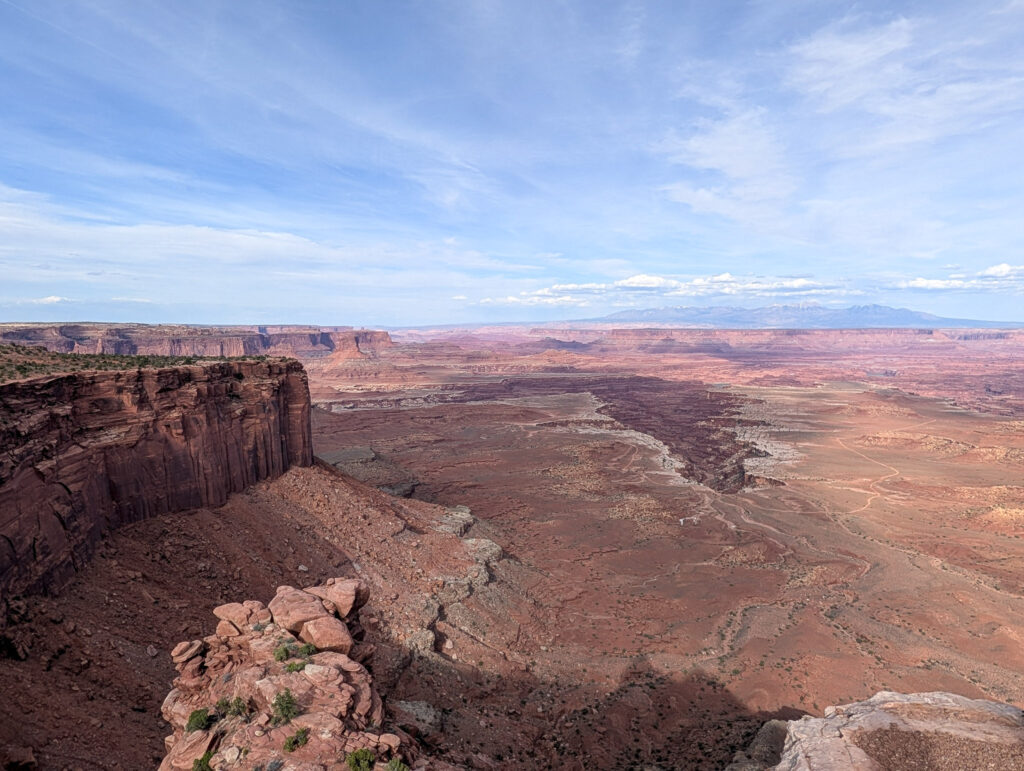 Golden-hour view from Buck Canyon Overlook in Canyonlands, with sheer red sandstone cliffs and the La Sal Mountains on the horizon.