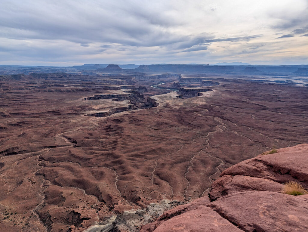 View from Green River Overlook in Canyonlands, where the river winds as a silver thread through eroded red rock canyons under heavy overcast skies.