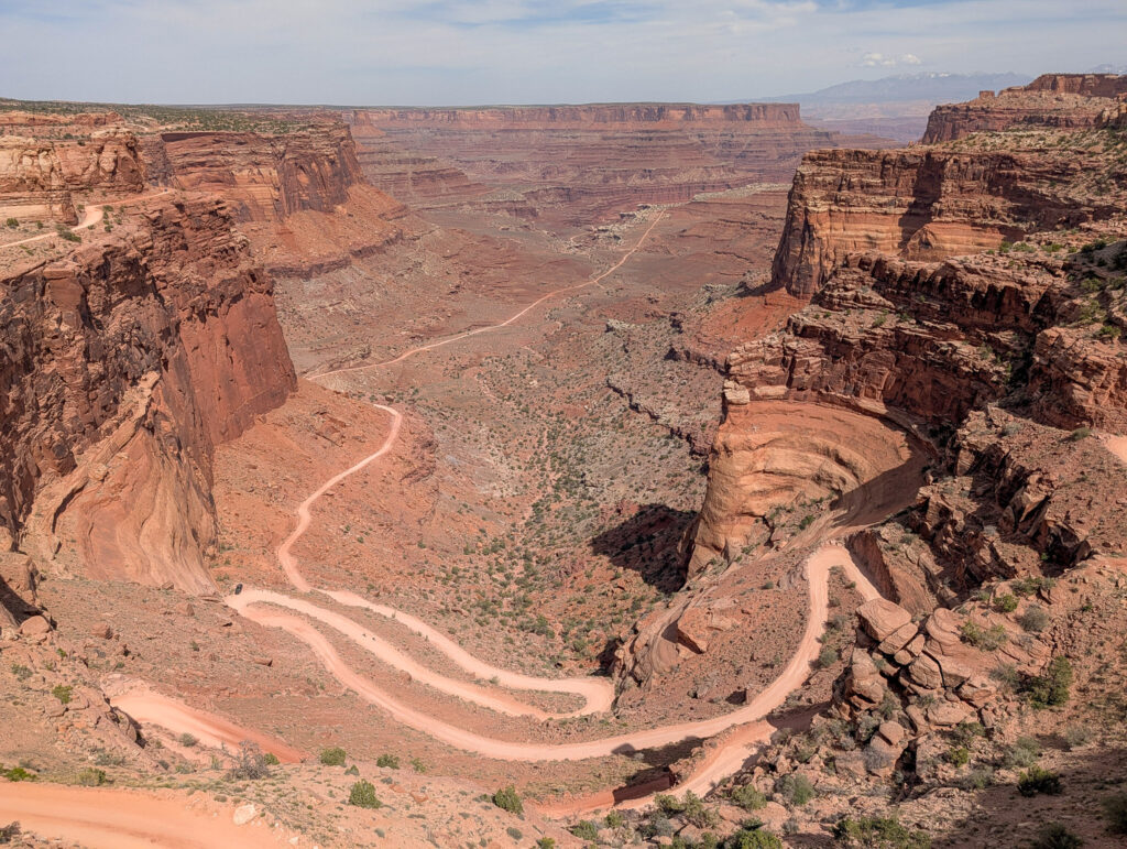 Aerial view of Shafer Trail's tight switchbacks descending from Island in the Sky mesa into Shafer Canyon, with the La Sal Mountains on the horizon.