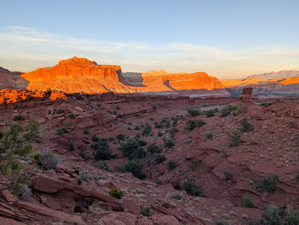 Wide view from Sunset Point overlooks the layered red sandstone mesas of the Waterpocket Fold, with the snow-capped Henry Mountains on the horizon.