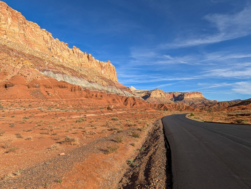 Capitol Reef Scenic Drive curves past towering Waterpocket Fold cliffs glowing warm in late-day light under a vivid blue sky.
