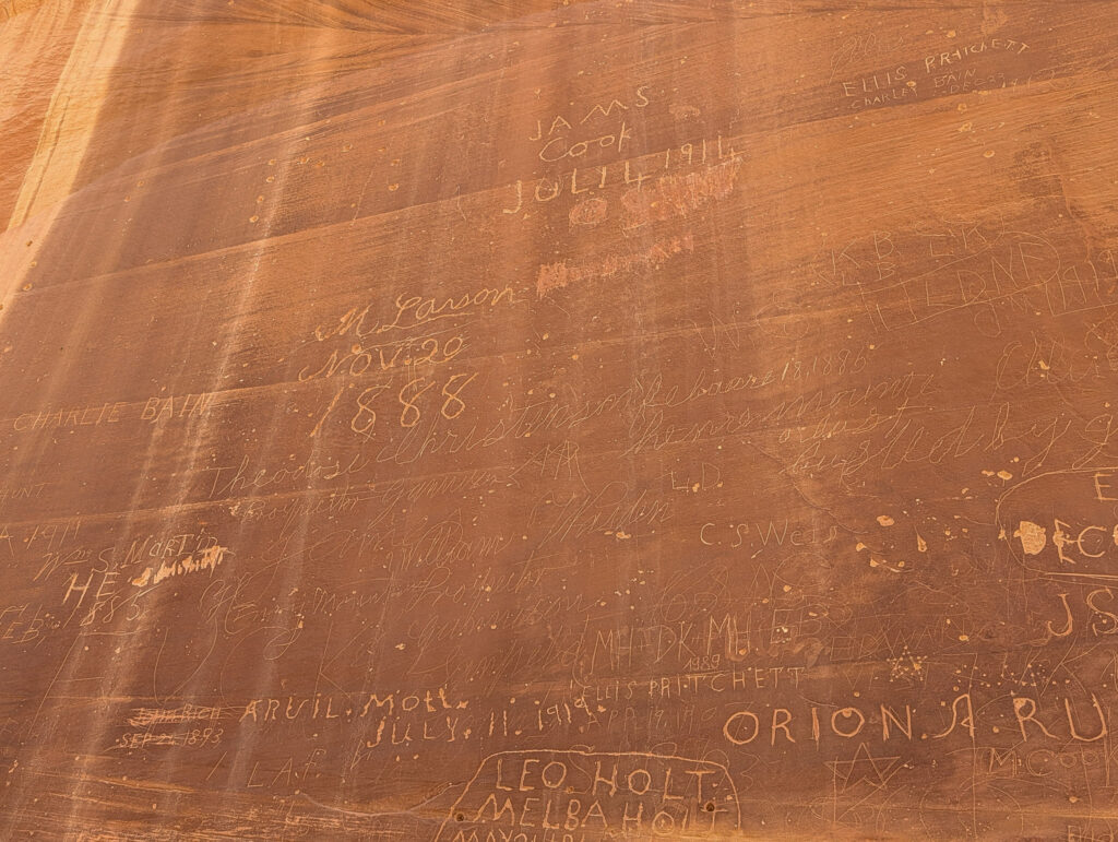 Newspaper Rock at Capitol Reef National Park, its sandstone face densely carved with pioneer names and dates, lit by warm golden sidelight.