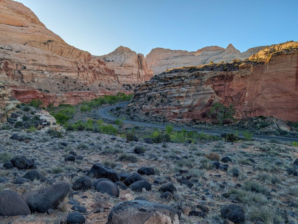 Capitol Reef Scenic Drive winds through the Fremont River gorge, flanked by layered red and cream Navajo sandstone cliffs under a clear midday sky.