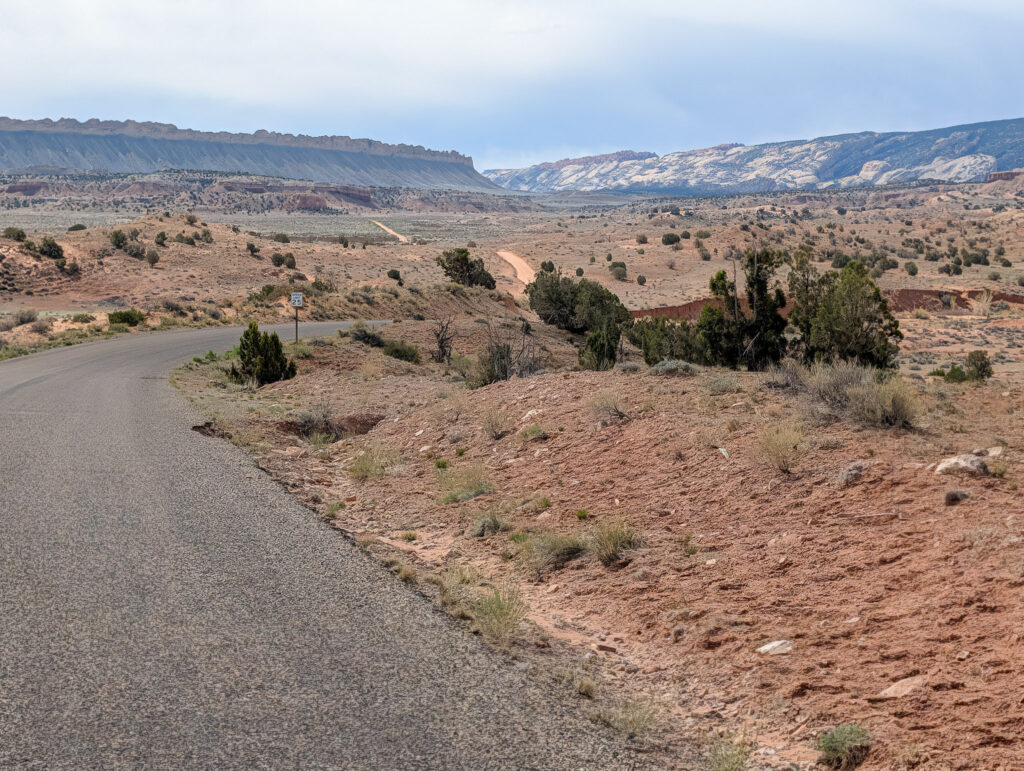 Cottonwood Canyon Road descends into a broad red-rock valley in Grand Staircase-Escalante, with sedimentary ridges visible under an overcast sky.