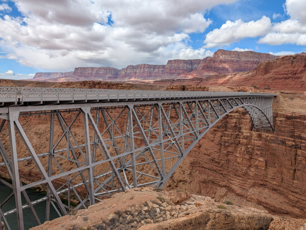 Twin steel arch spans of Navajo Bridge cross Marble Canyon above the Colorado River, with red Vermilion Cliffs rising behind.