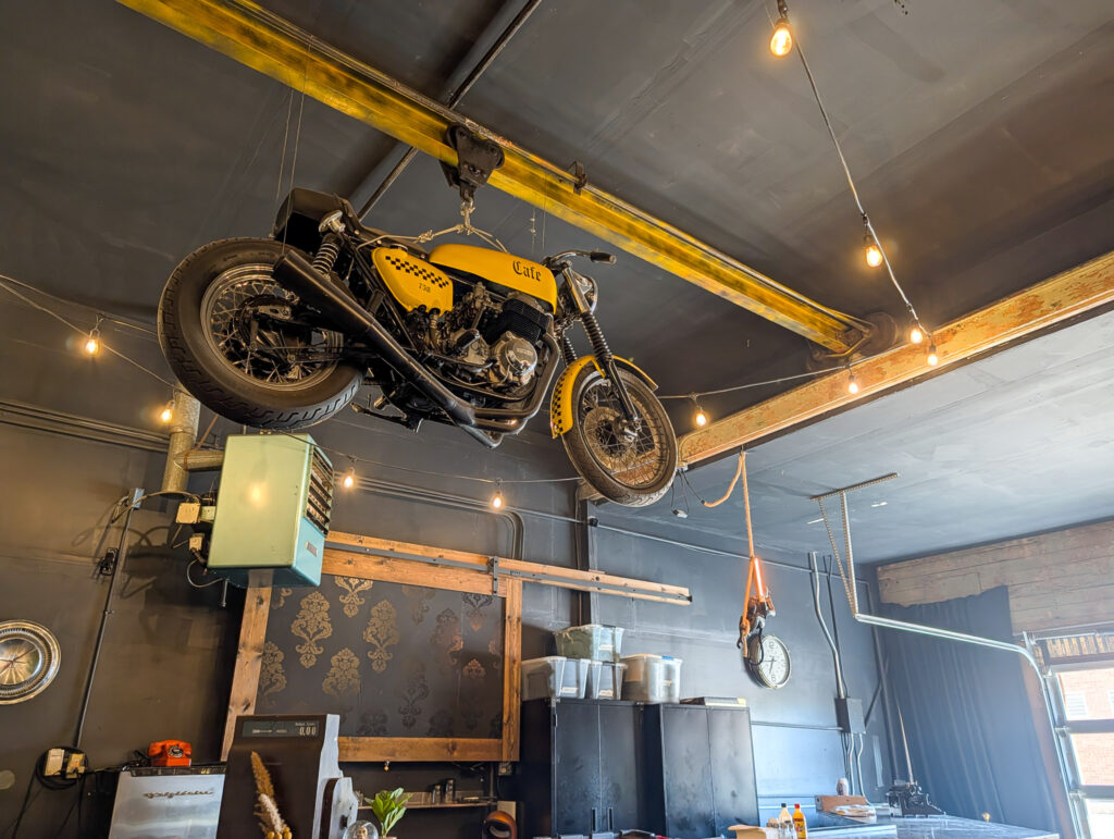 A yellow cafe-racer motorcycle suspended from a gantry crane beam inside Cafe 730 in Moab, Utah.