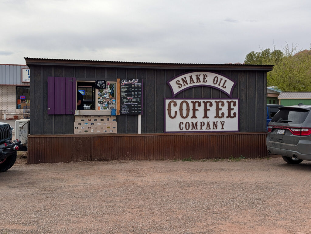 Exterior of Snake Oil Coffee Company in Moab, a small drive-thru shack with dark board-and-batten siding and a purple-shuttered service window.