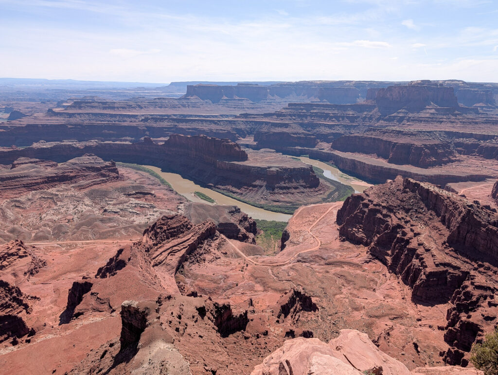 Wide view from Dead Horse Point overlook of the Colorado River's sweeping gooseneck bend cutting through layered red canyon walls below.