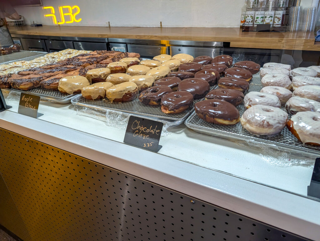 Display case filled with maple-glazed, chocolate-glazed, and white-glazed ring donuts at a Moab donut shop.