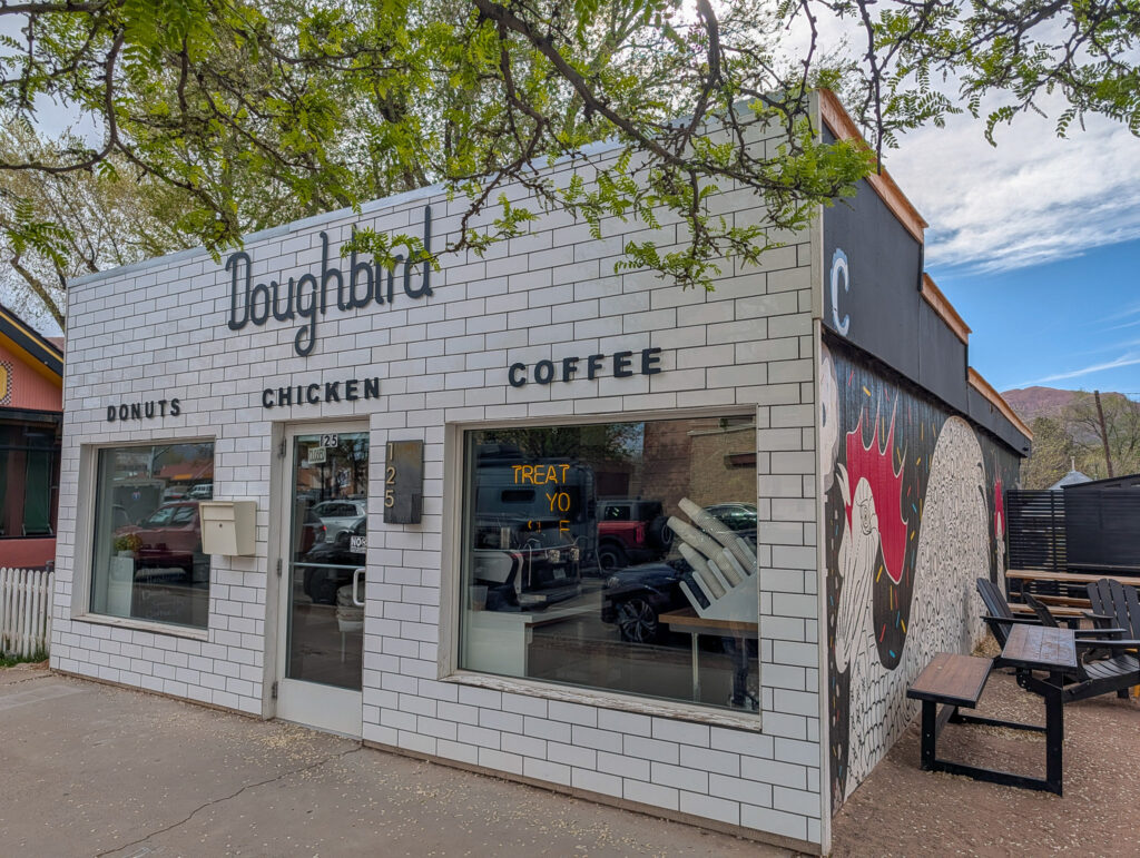 Doughbird's white subway-tile storefront in Moab glows in evening light, with a colorful donut mural and outdoor seating visible.