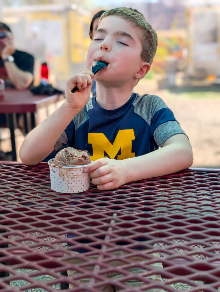 Young boy in a University of Michigan jersey savoring chocolate ice cream at an outdoor table in Moab.
