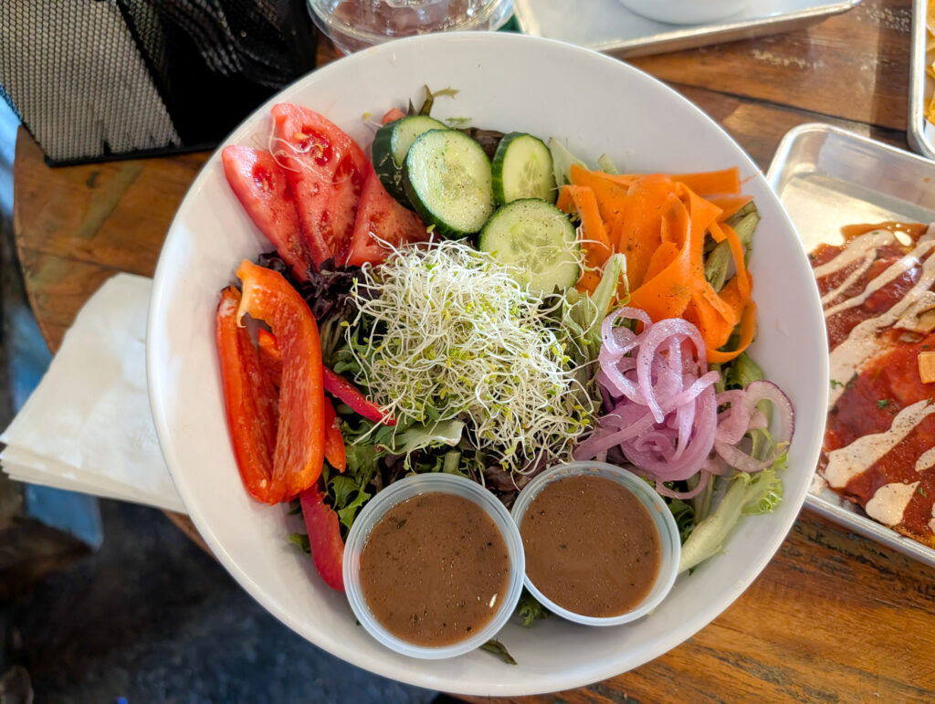 Overhead view of a large white bowl salad with mixed greens, sprouts, tomatoes, cucumber, carrots, and balsamic dressing at a Moab restaurant.