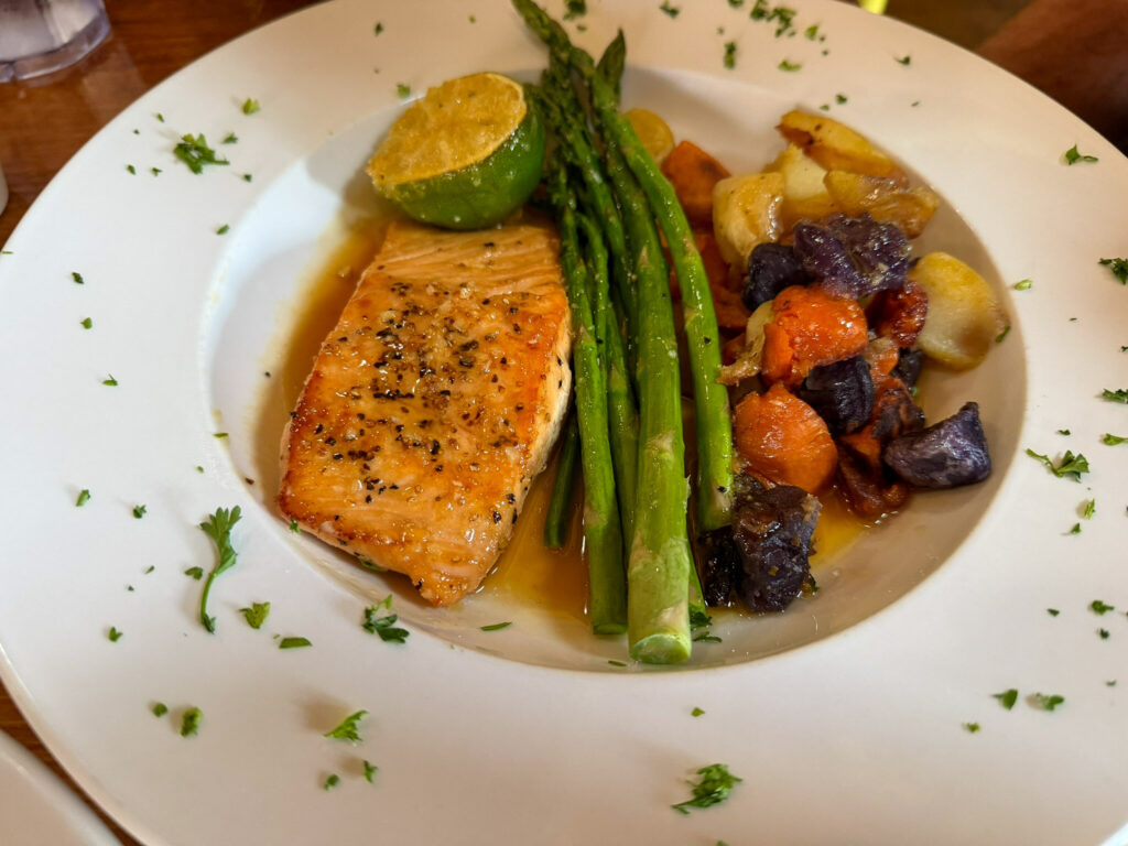 Pan-seared salmon fillet with asparagus, roasted tri-color potatoes, carrots, and halved lime on a white plate.