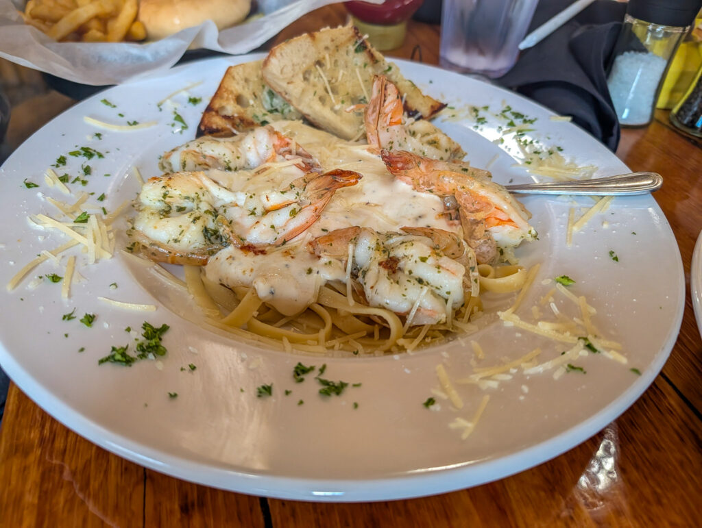 A white plate piled with shrimp scampi linguine in garlic butter sauce, topped with parmesan and served with garlic bread at a Moab restaurant.