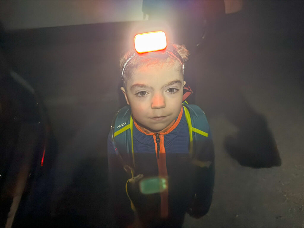 Young child with glowing headlamp and Osprey pack looks up during a foggy nighttime hike near Moab.