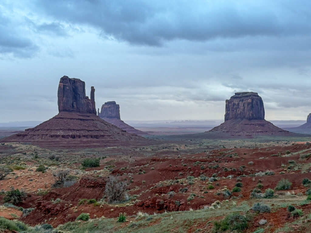 West and East Mitten Buttes rise from the red desert floor at Monument Valley under a brooding, storm-filled sky.