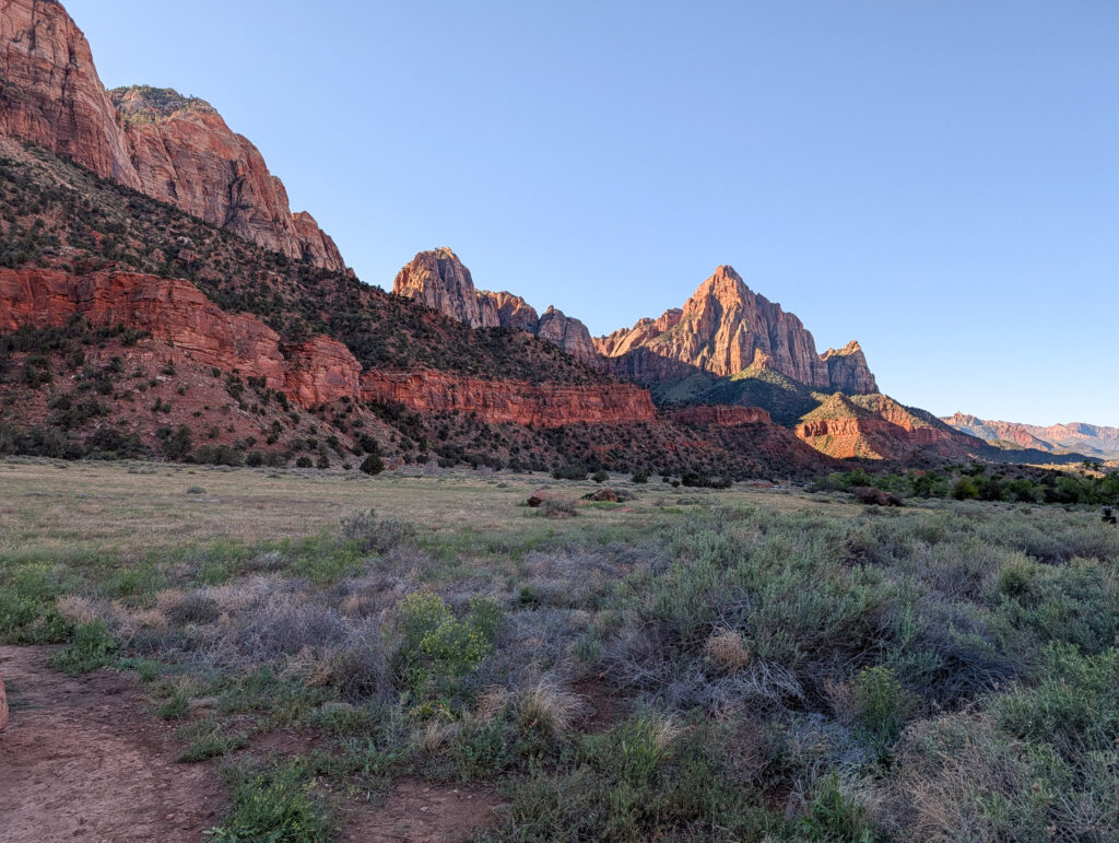 The Watchman rises above the sagebrush flats near Zion's south entrance, flanked by layered Navajo sandstone cliffs under a clear midday sky.