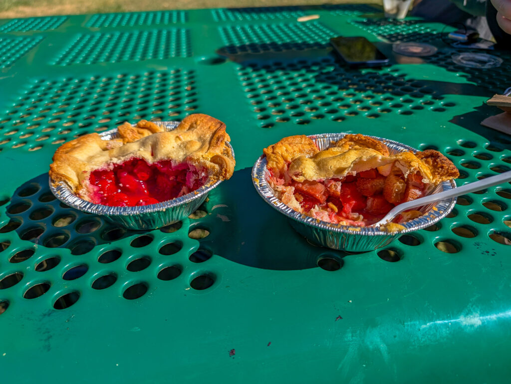 Two mini fruit pies, sliced open to reveal cherry and peach fillings, sit on a green steel picnic table outside the Gifford House.
