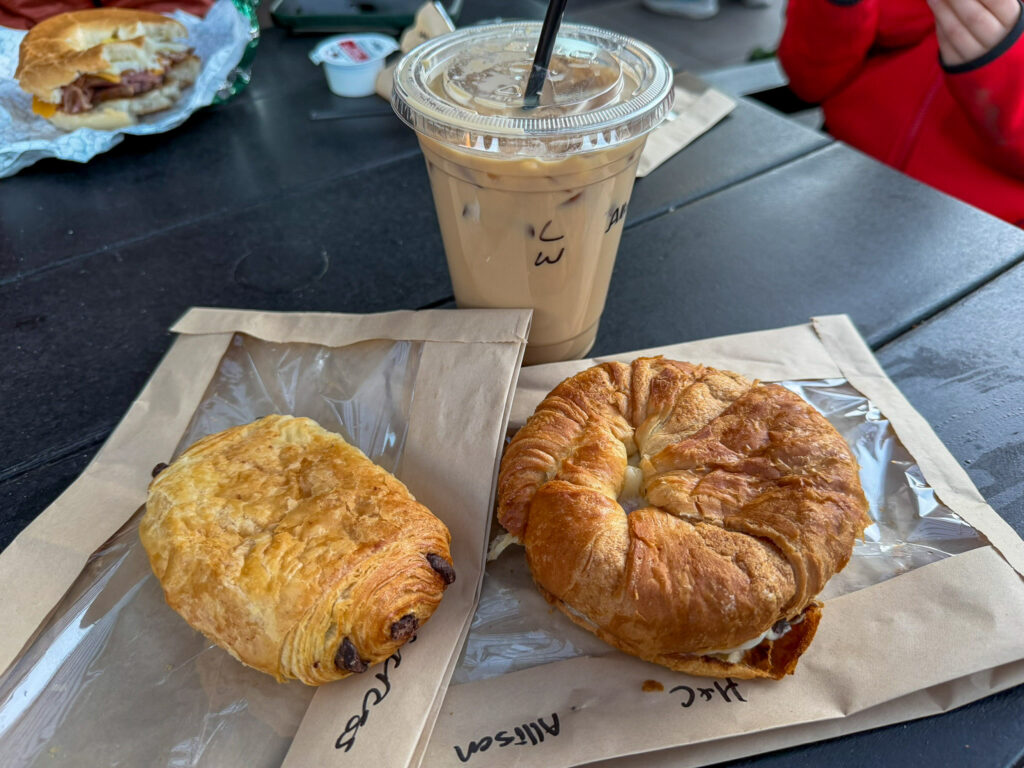 A chocolate croissant and a butter croissant on parchment with an iced latte on the Canyon Coffee outdoor patio table in Springdale, Utah.