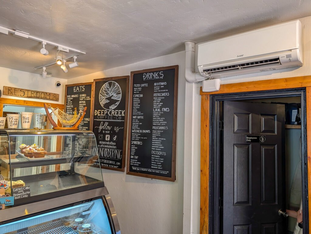Interior of Deep Creek Coffee in Springdale, Utah showing the chalkboard eats and drinks menus on the wall, a pastry case below, and the kitchen door beside the menu boards.
