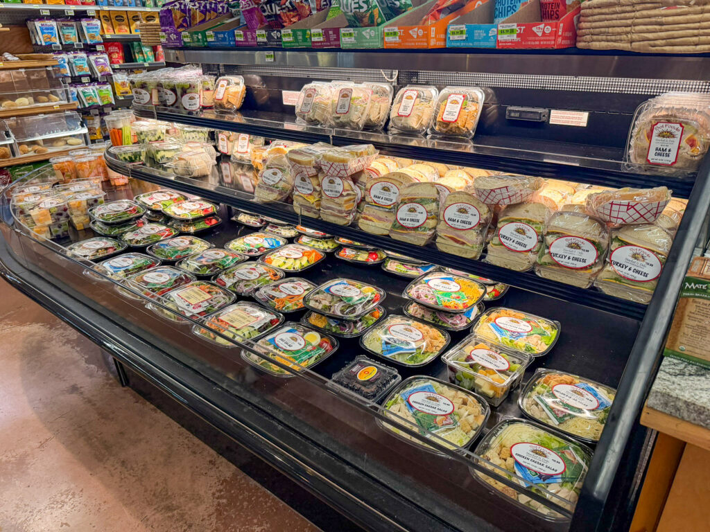 Refrigerated deli case at Sol Foods Supermarket in Springdale, Utah filled with prepared sandwiches, wraps, and salad containers ready for grab-and-go customers.