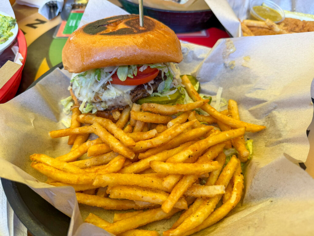 A cheeseburger with lettuce and tomato on a brioche bun served with a generous basket of seasoned French fries at Oscar's Cafe in Springdale, Utah.