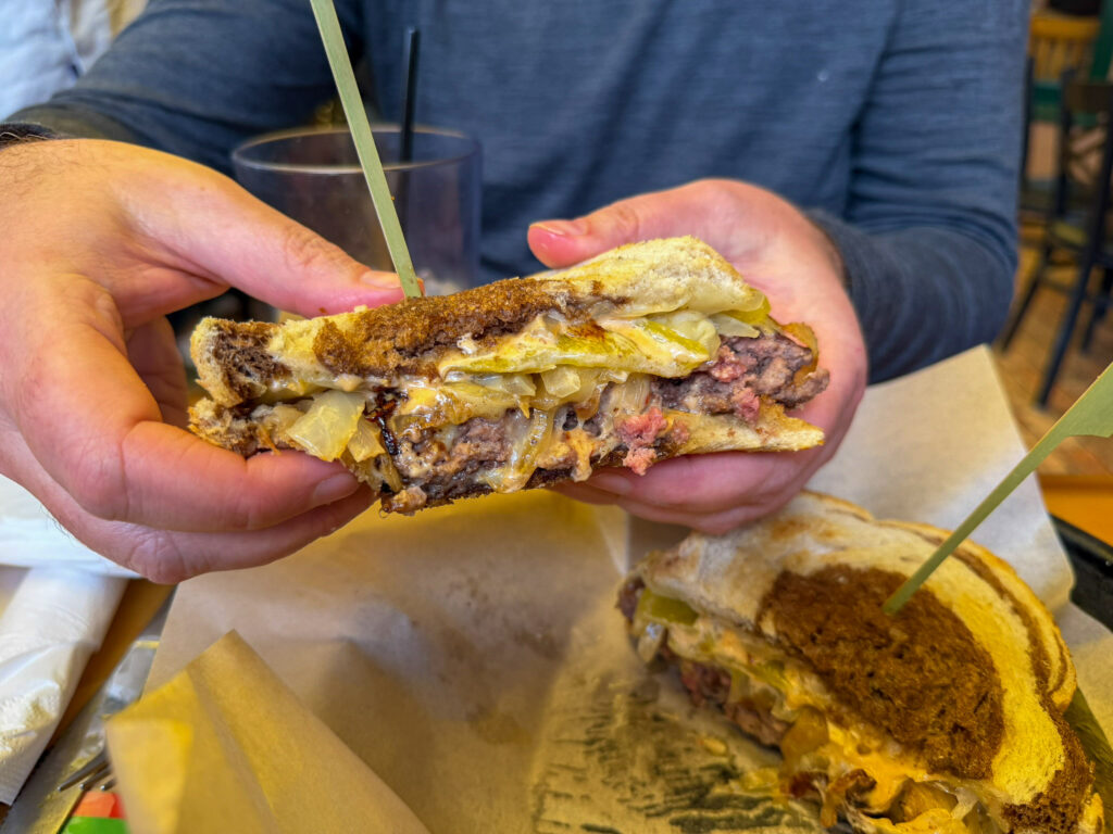 A patty melt at Oscar's Cafe in Springdale, Utah held up to show the cross section with melted cheese, grilled onions, and a thick beef patty on toasted marble rye bread.