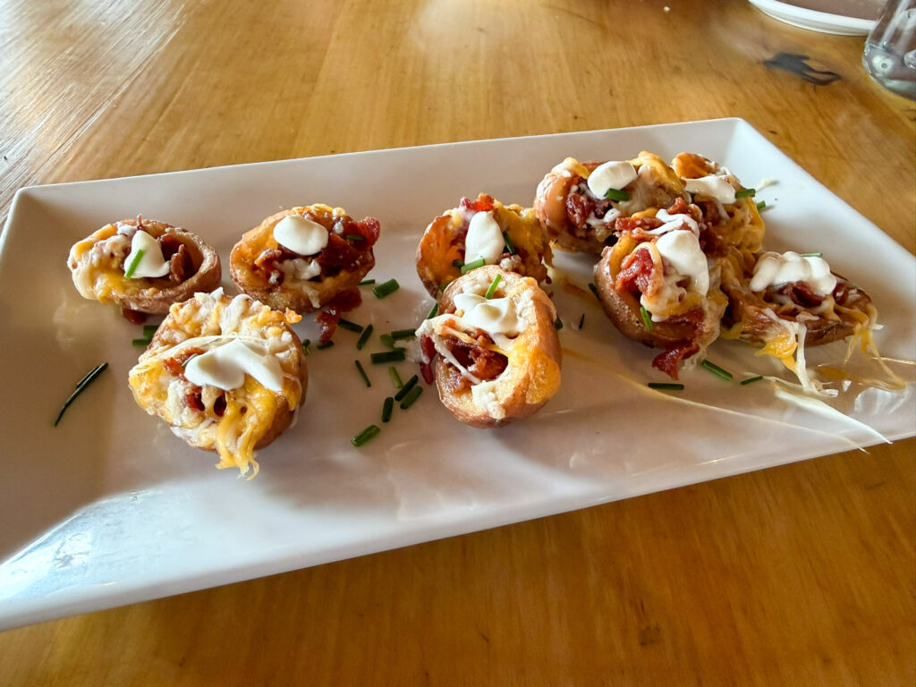 Loaded potato skins topped with melted cheese, bacon, sour cream, and chives on a white rectangular plate at Broken Spur Inn restaurant in Torrey, Utah.