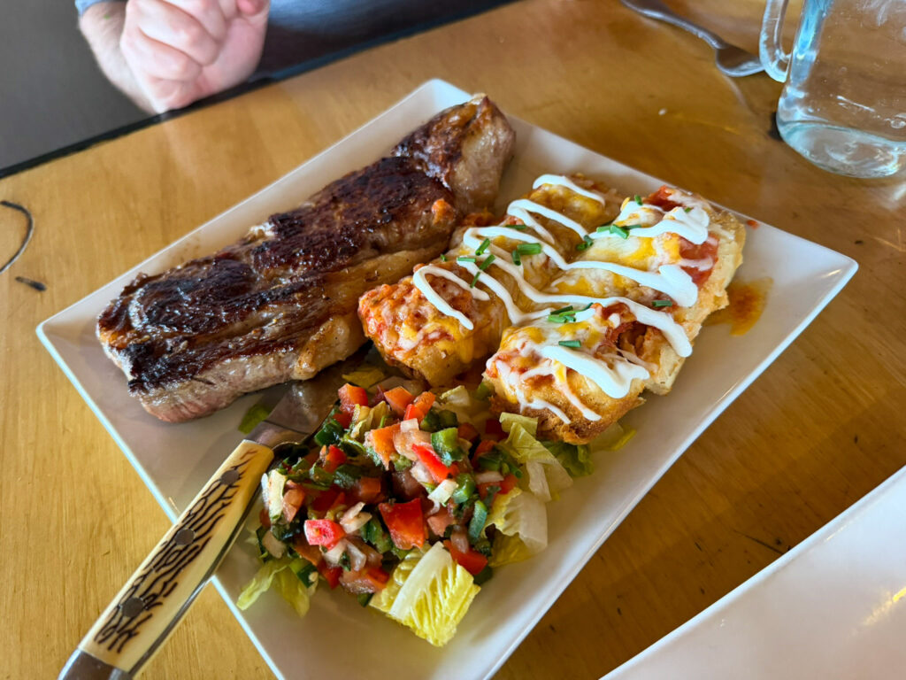 Grilled steak served alongside cheese-topped enchiladas and a side of fresh pico de gallo on a white plate at Broken Spur Inn restaurant in Torrey, Utah.