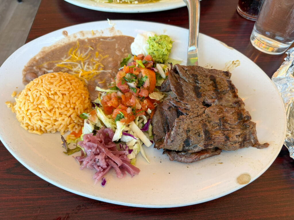 A grilled carne asada steak plated with Mexican rice, refried beans, pico de gallo, guacamole, and pickled onions at Chak Balam restaurant in Torrey, Utah.