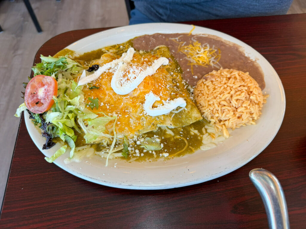 Cheese-topped enchiladas verdes drizzled with crema and served with Mexican rice, refried beans, and a side salad on an oval plate at Chak Balam restaurant in Torrey, Utah.