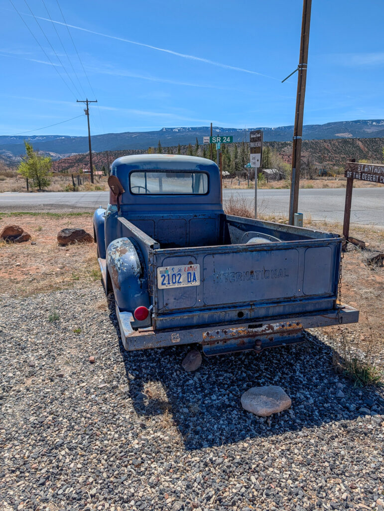 Rear view of a weathered vintage blue International pickup truck parked along the roadside near Chak Balam restaurant in Torrey, Utah, with the Capitol Reef cliffs in the distance.