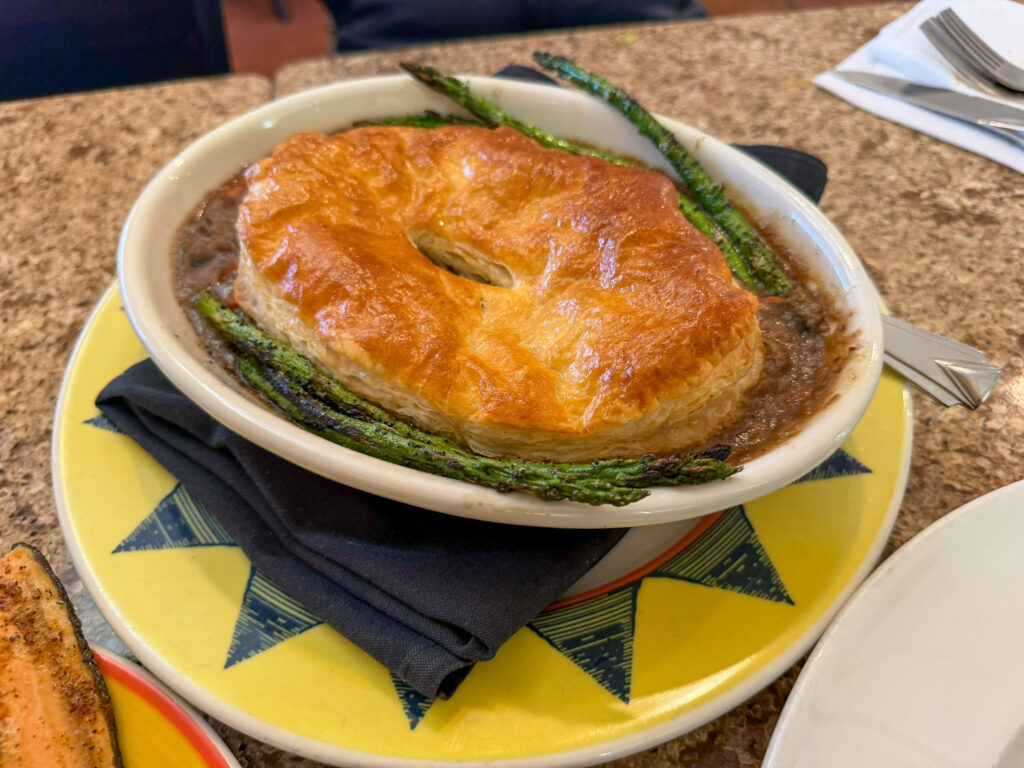 A puff-pastry-topped pot pie in an oval bowl garnished with roasted asparagus spears at Hunt and Gather restaurant in Torrey, Utah.