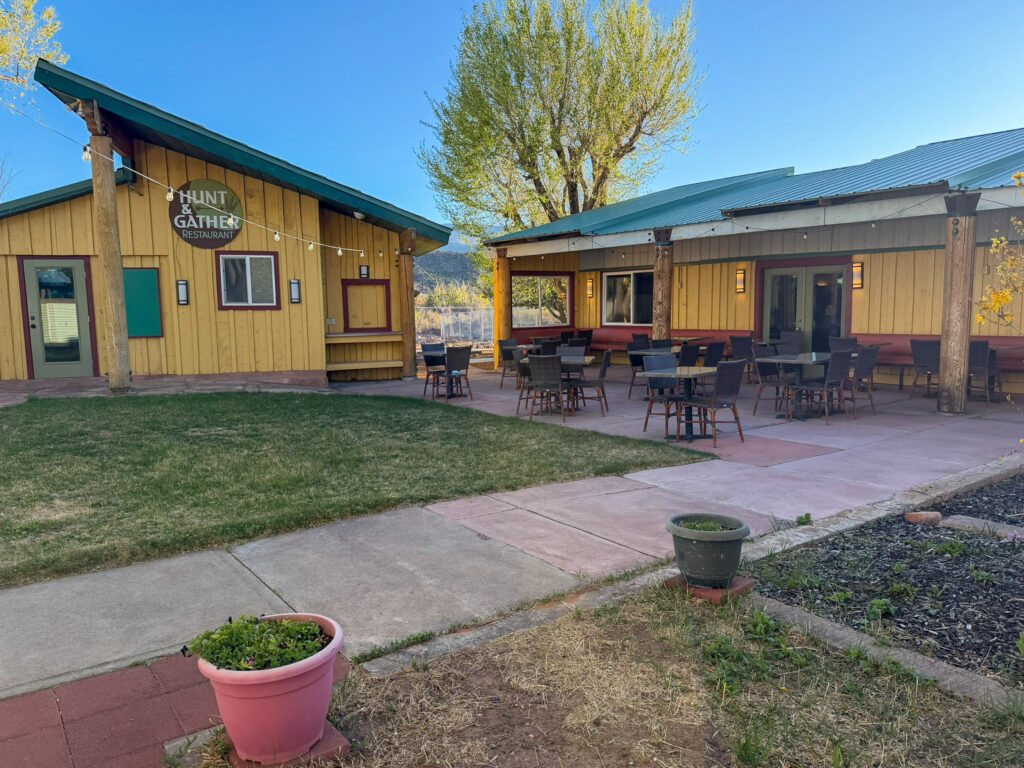 Exterior view of the yellow Hunt and Gather restaurant buildings with an outdoor patio and tables beneath a string of lights in Torrey, Utah.