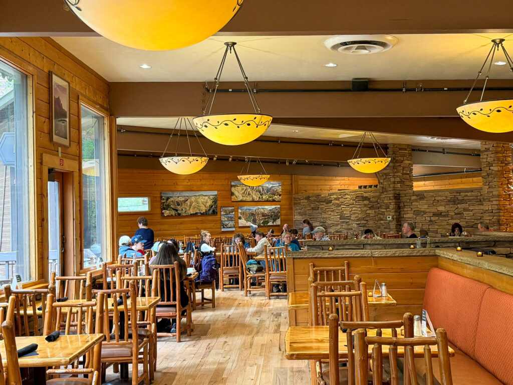 Glowing yellow pendant lights hang above wooden tables and the bar inside the warm Red Rock Grill dining room at Zion Lodge.
