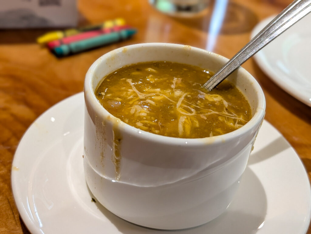 A white ceramic cup brimming with hearty green chile chicken soup served on a saucer at the Red Rock Grill inside Zion Lodge.