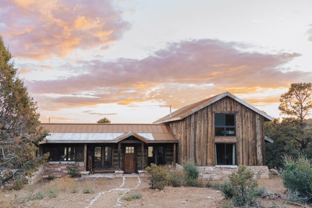 Zion Mountain Ranch in Orderville, Utah, a rustic log-and-stone lodge building framed by desert shrubs and junipers beneath a vivid pink-and-gold sunset sky.