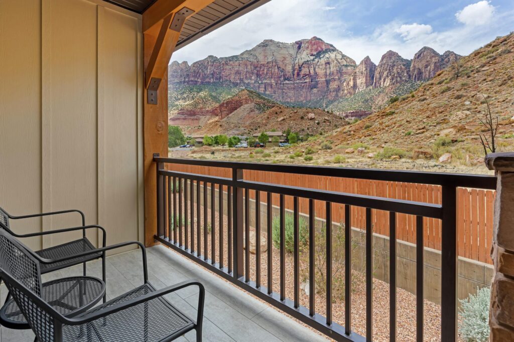 A covered balcony at Best Western Plus in Springdale, Utah, with two chairs overlooking scrubland and red sandstone canyon walls rising beyond the property.