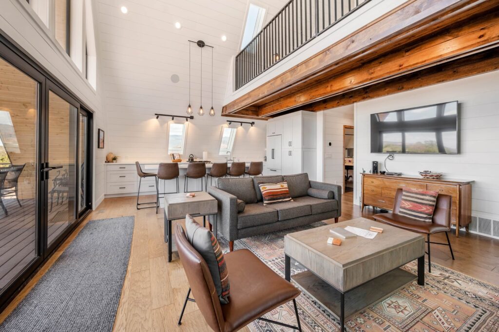 Interior of a Cabins at Capitol Reef cabin in Torrey, UT, featuring a vaulted shiplap ceiling with wood beams, a loft, cozy living area with Southwestern accents, open kitchen, and sliding glass doors to a deck.