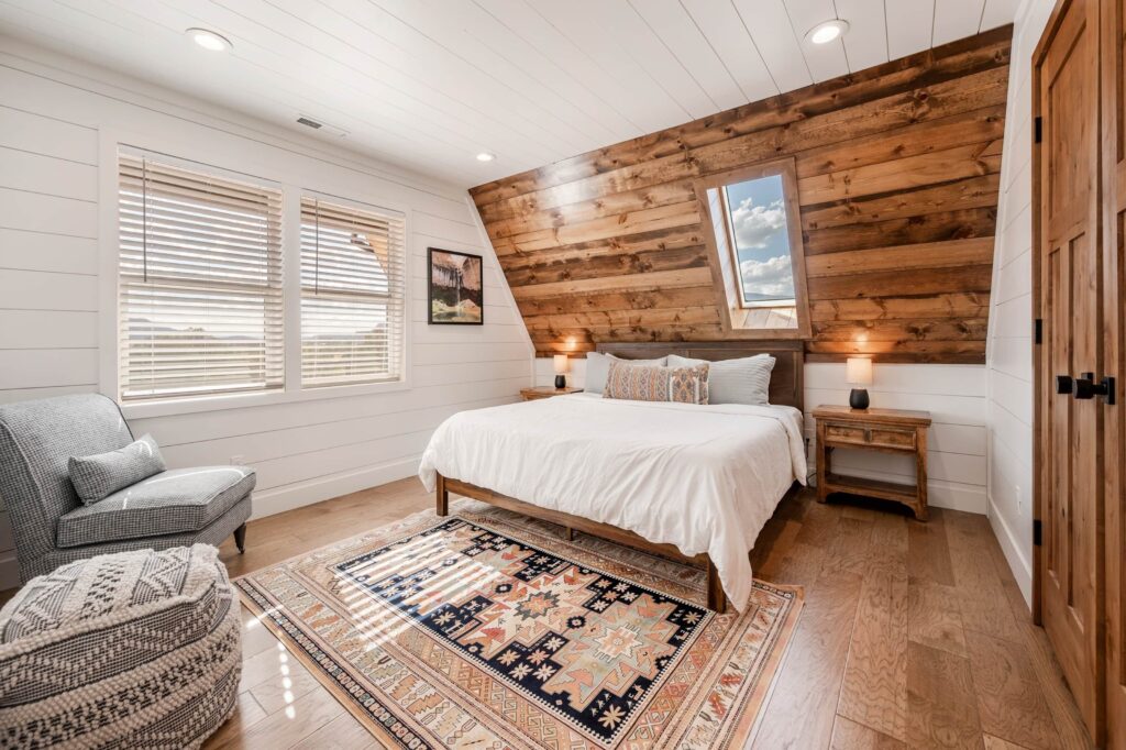 Loft bedroom in a Cabins at Capitol Reef lodging featuring a king bed beneath a skylight, warm wood accent wall, shiplap, and southwestern-style décor in Torrey, UT.