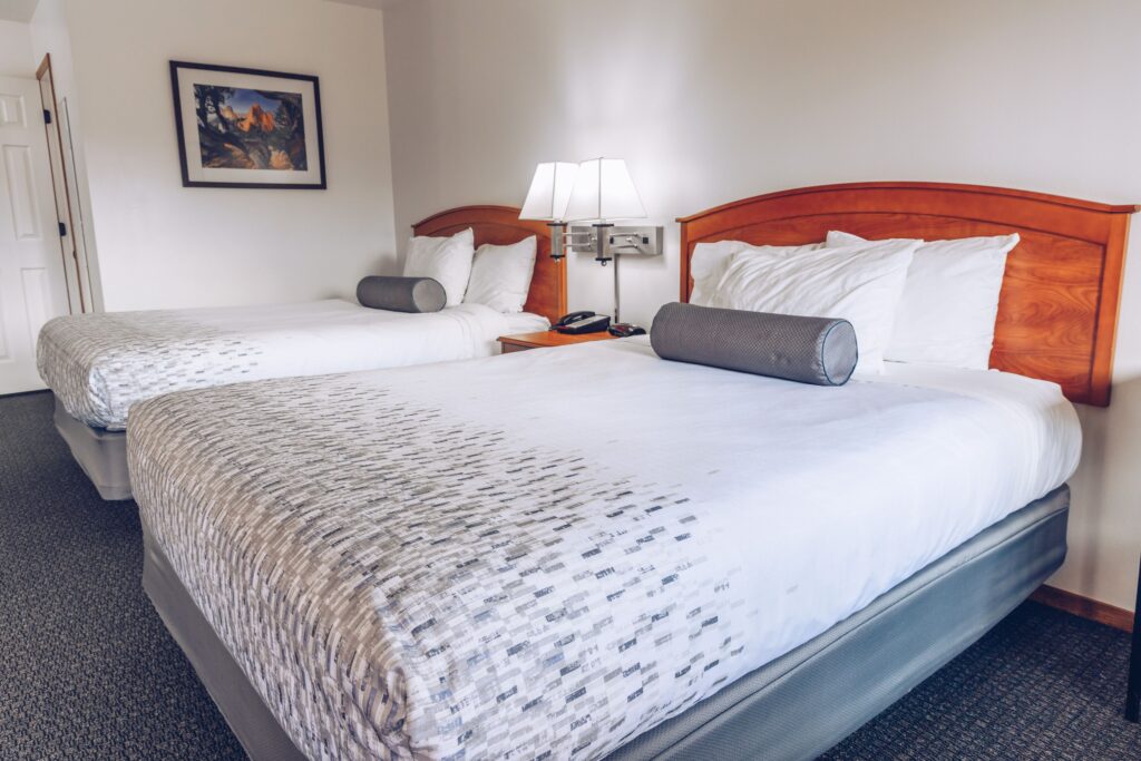 Chuckwagon Lodge guest room in Torrey, UT with two queen beds, wood headboards, gray patterned spreads, and a shared nightstand with lamp between them.